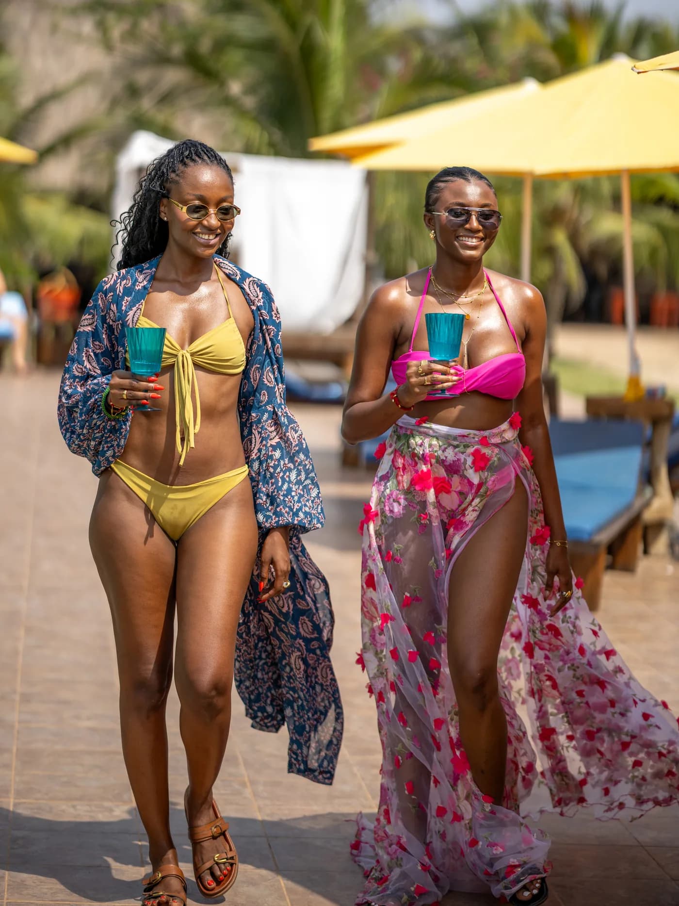Two guests walking through the grounds with drinks, yellow umbrellas behind them