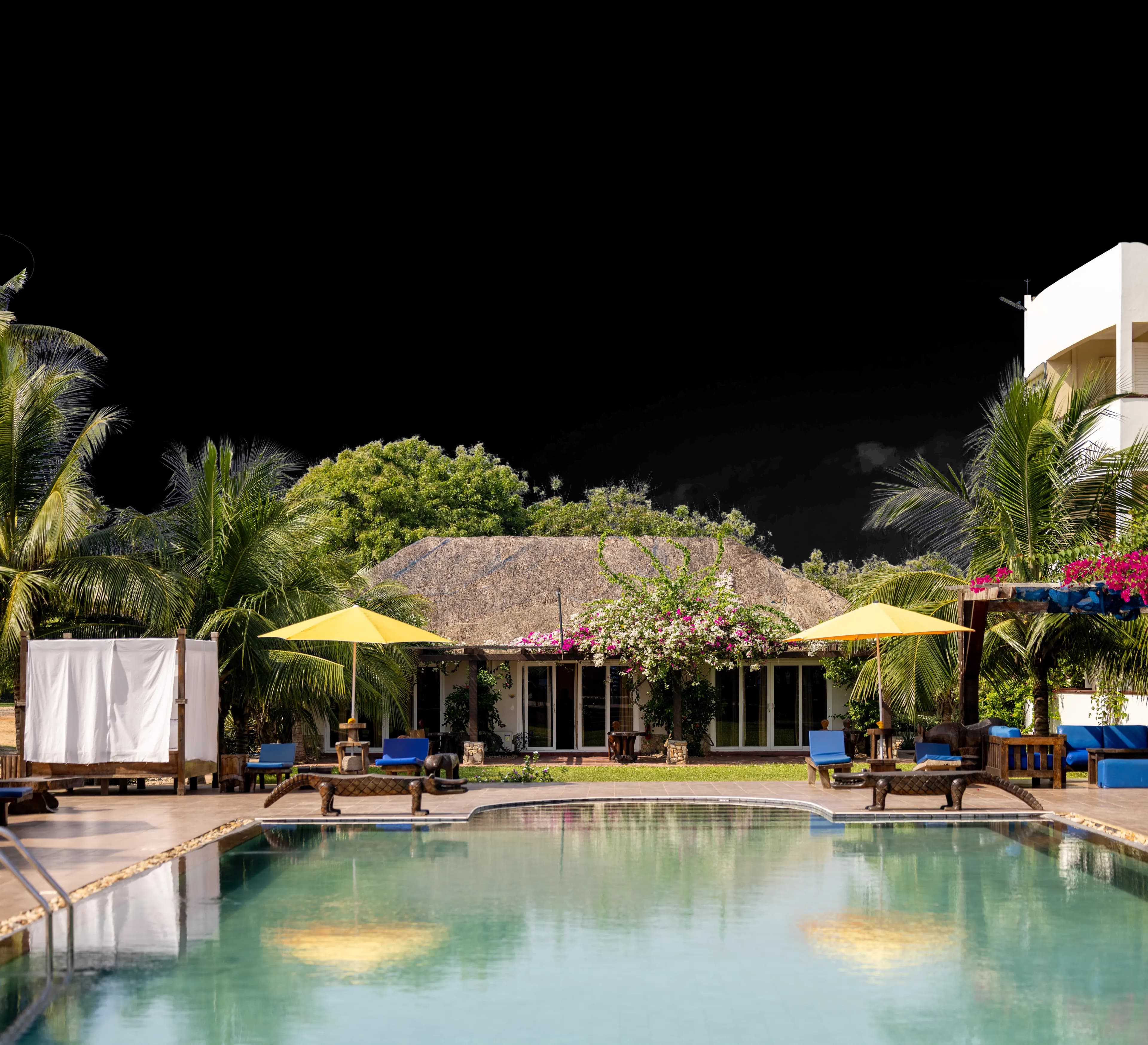 The main pool in daylight, the thatched restaurant behind it, bougainvillea over the roof