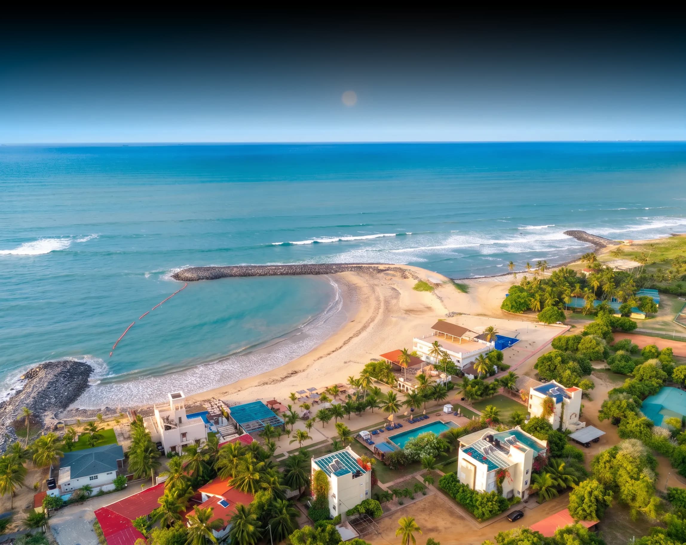 The cove, the sea defence and the resort from the air, the Atlantic running out to the horizon