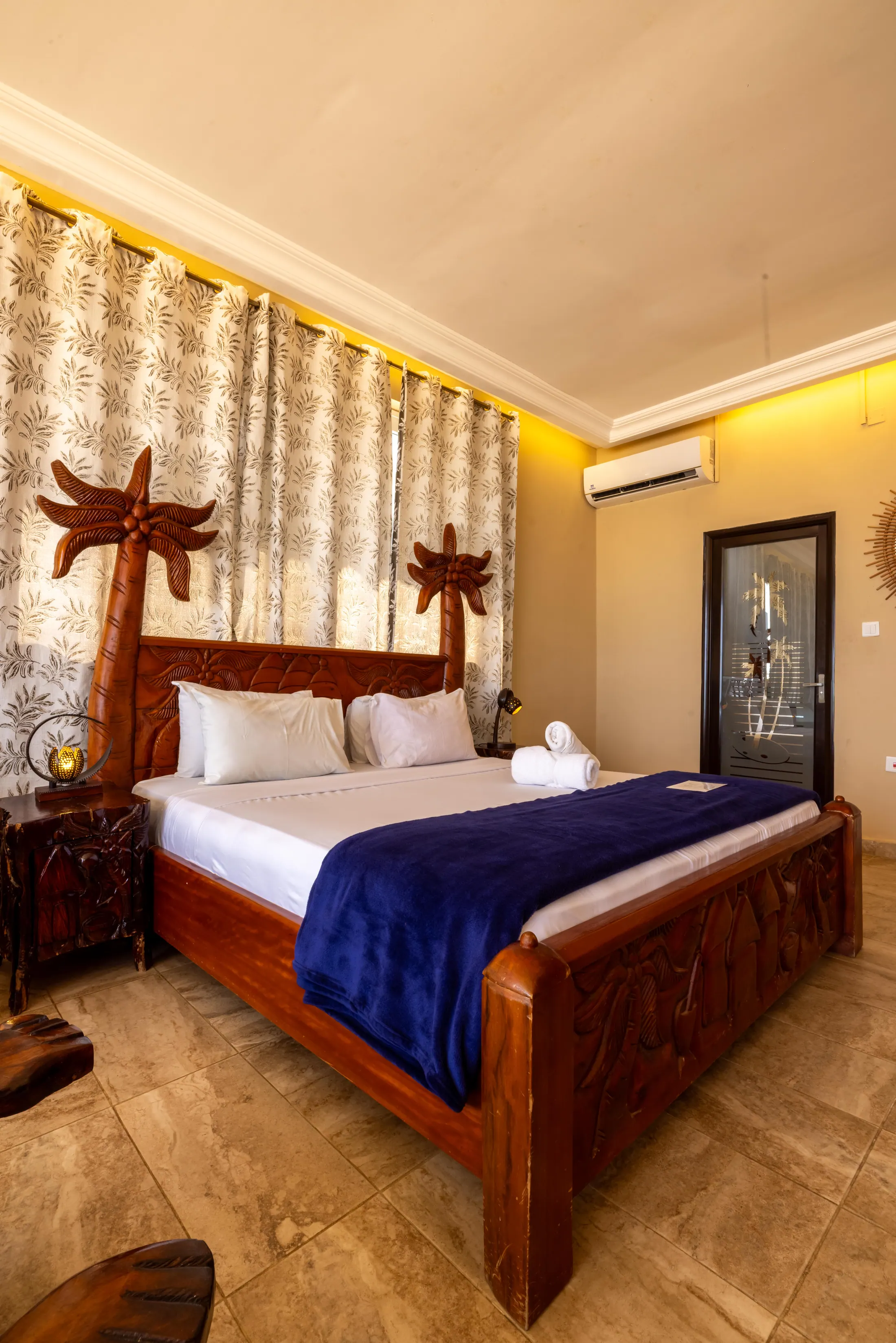 A guest room with carved bedposts and a Ghanaian canvas on the wall